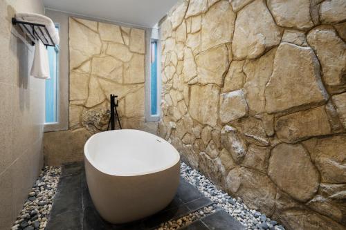 a bathroom with a stone wall and a bath tub at Myze Hotel Waingapu in Waingapu