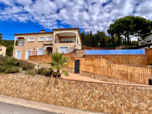 a house behind a stone wall with a palm tree at Casa Mas Ambros con piscina desbordante in Calonge