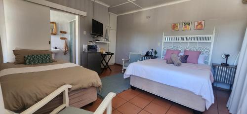 a bedroom with two beds and a kitchen in the background at RoomsAtRoseAve19 in Kuruman