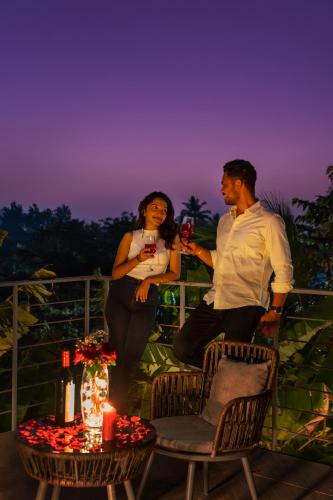 a man and a woman standing on a balcony with drinks at SaffronStays Eden - 3BR vineyard-side pool villa with jacuzzi, farm dining, stargazing deck & lawns for celebrations in Nashik