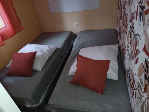 two beds in a small room with red and white pillows at Mobil home paisible in Saint-Chéron