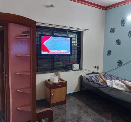 a person laying on a bed in a bedroom with a television at Saraswati Sadan in Hospet
