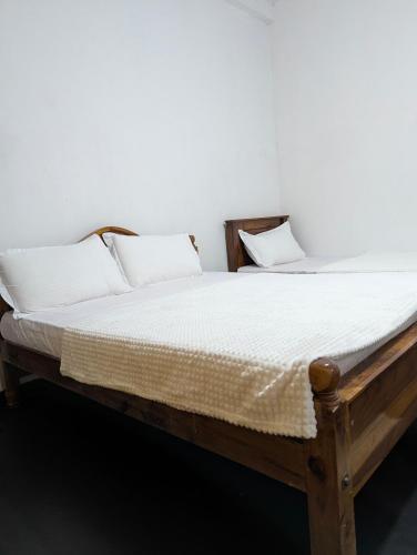 a wooden bed with white sheets and pillows at Senaya Homestay in Belihuloya