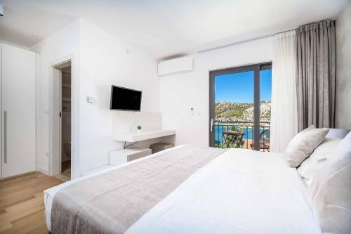 a white bedroom with a large bed and a tv at Villa High Life in Seget Vranjica