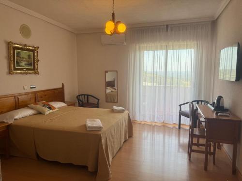 a bedroom with a bed and a desk and a window at Hotel Dracos in Cebreros