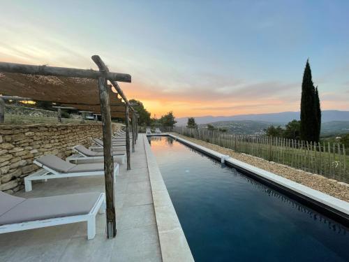 a pool with lounge chairs and a sunset in the background at Domaine des Druides in Apt