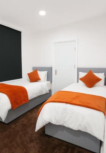 two beds with orange and white sheets in a bedroom at Lincoln Manor 5BR in Peterborough