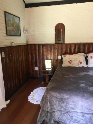 a bedroom with a bed and a table with a lamp at Passarim Chalé in Monte Verde