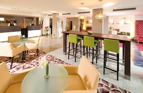 a lobby with a bar with green chairs and tables at Leonardo Hotel Hannover Airport in Hannover