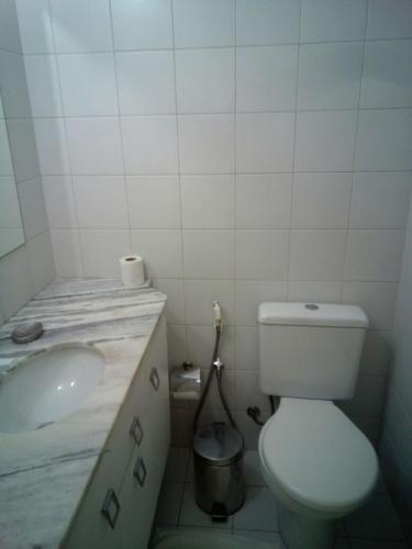 a white bathroom with a toilet and a sink at Apartamento Enseada Praia do Forte in Praia do Forte