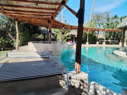 a swimming pool with two beds and a wooden umbrella at Ashly Loma Larga in Acapulco