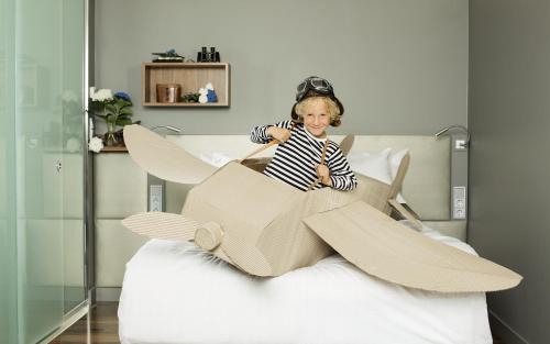 a young child sitting in a cardboard airplane on a bed at GLO Hotel Airport in Vantaa