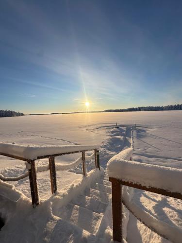 two benches covered in snow with the sun in the background at Lapland Heritage Villa in Ranua