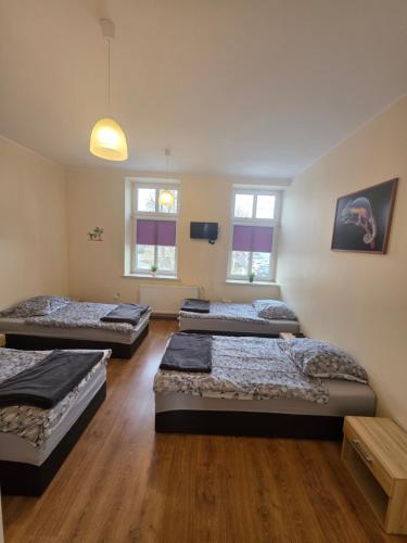 three beds in a room with wooden floors and windows at Noclegi Społem in Będzin
