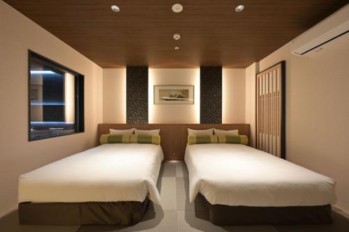 two twin beds in a room with a window at HOTEL THE7 Kumamoto in Kumamoto