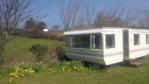 a white trailer parked in a field with flowers at Caravan by Sea in Morfa Nefyn