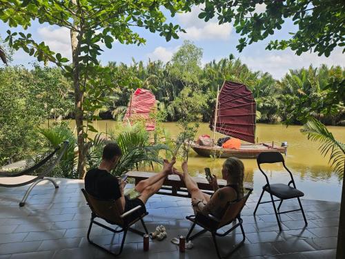 a man and woman sitting at a table with their legs in the air at Comfy room - InnerZen Mekong Riverside homestay Ben Tre in Ben Tre