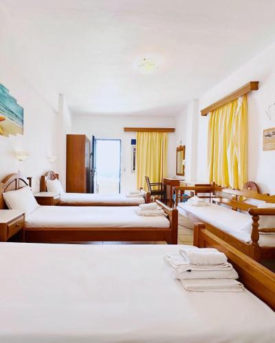 a room with several beds and tables and yellow curtains at Hermes-Ios Rooms To Let in Ios Chora