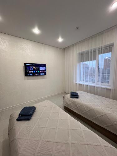 a bedroom with two beds and a tv on the wall at Welcome Hotel in Kostanay