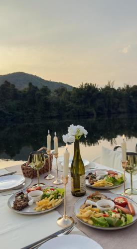a table with plates of food and a bottle of wine at Heaven Raft Erawan Floating Resort Romantic River View in Ban Mong Lai