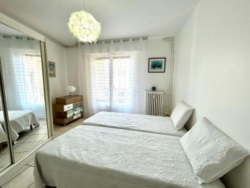 a white bedroom with two beds and a chandelier at Le Catalogne 3 in Perpignan