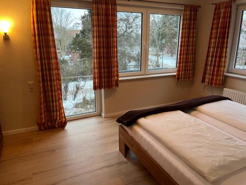 a bedroom with a bed and two large windows at Haus Seeschwalbe - Wohnung 07 in Spiekeroog