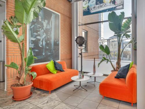 two orange couches sitting in a room with plants at B&B HOTEL Milano Cologno Studios in Cologno Monzese