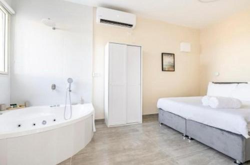 a white bedroom with a tub and a bed and a bath tub at וילה קלמה מגדל in Migdal