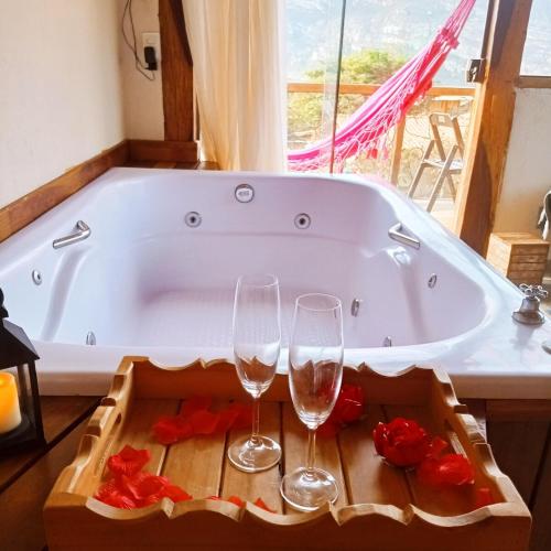 a bath tub with two glasses of wine and roses at Chalé com Jacuzzi vista para Pico da Lapinha in Santana do Riacho