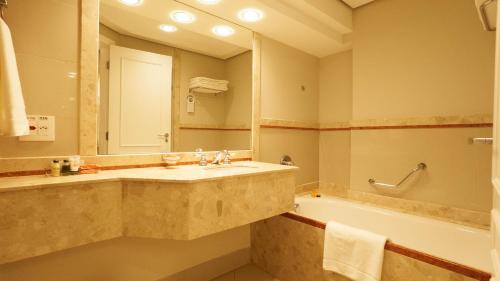 a bathroom with a sink and a tub and a mirror at Royal Palm Plaza Resort in Campinas