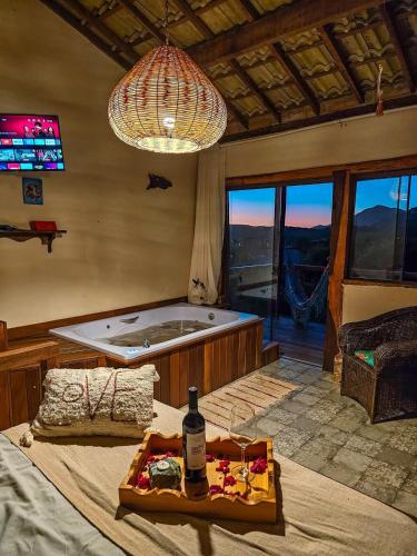 a bedroom with a tub and a table with a bottle of wine at Chalé com Jacuzzi vista para Pico da Lapinha in Santana do Riacho