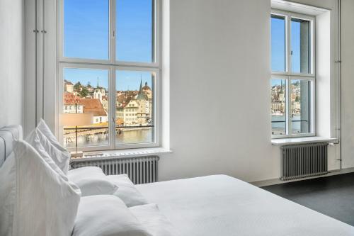 a white bedroom with a bed and two windows at Starlight Loft Lucerne, World Above Chapel Bridge in Lucerne