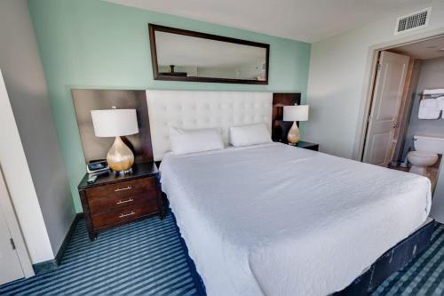 a bedroom with a white bed and two lamps and a mirror at Seaside condo w hot tub & private balcony in Myrtle Beach