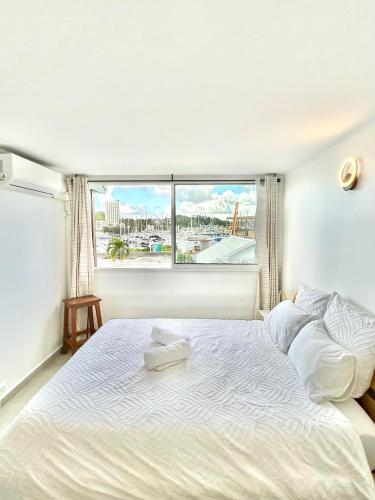 a bedroom with a large white bed with a window at Vue mer sur la Marina, Le Juliana in Pointe-à-Pitre