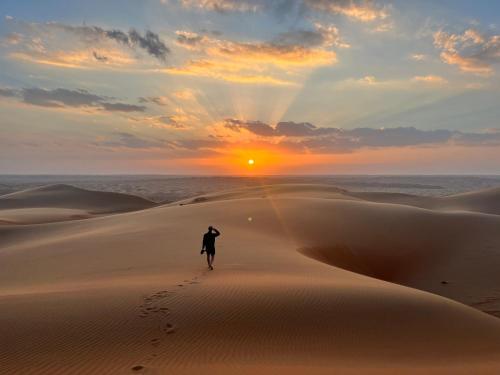 osoba spacerująca po pustyni o zachodzie słońca w obiekcie Quiet Nights Camp w mieście Badīyah
