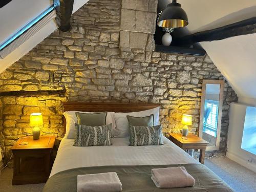 a bedroom with a stone wall with a bed and two lamps at Priory Weavers Cottage in Burford