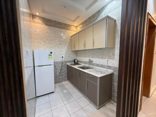 a small kitchen with a white refrigerator and cabinets at شاليهات وشقق ليالي رهيف in Abha
