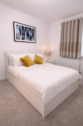 a white bedroom with a large white bed with yellow pillows at Ebbsfleet Luxe in Swanscombe