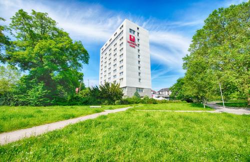 a tall white building with a red sign on it at Leonardo Hotel Karlsruhe in Karlsruhe