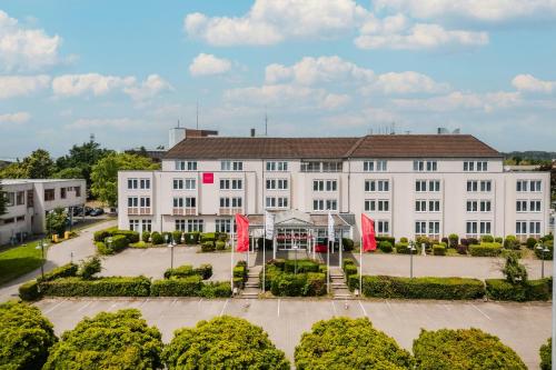 a large white building with red flags in front of it at Leonardo Hotel Aachen in Aachen