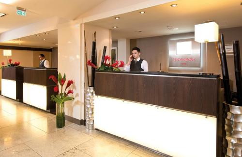 a reception desk in a hotel lobby with two men at Leonardo Hotel Hannover Airport in Hannover