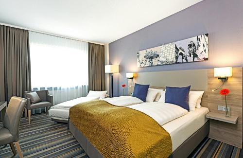 a hotel room with two beds and a chair at Leonardo Hotel Munich City North in Munich