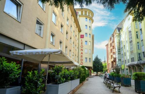 a street with benches and an umbrella in front of buildings at Leonardo Hotel Budapest in Budapest