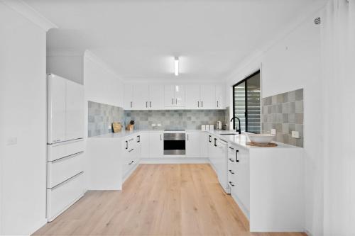 a white kitchen with white cabinets and a wooden floor at Baileys Beach House in East Ballina