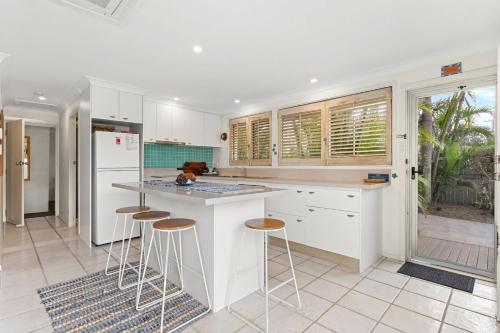 a kitchen with white cabinets and bar stools at Barefoot in Lennox in Lennox Head