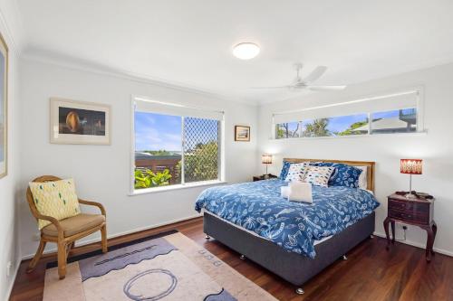a bedroom with a bed and a chair and two windows at Beach Views in Lennox Head