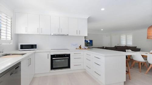 a white kitchen with white cabinets and a living room at Kay s Hideaway in Lennox Head