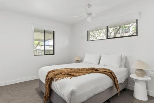 a bedroom with a bed with white walls and two windows at Lennox Beach Shack in Lennox Head