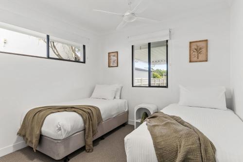 two beds in a room with white walls and windows at Lennox Beach Shack in Lennox Head