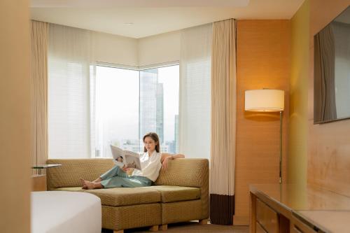 a woman sitting on a couch reading a book at Holiday Inn Bangkok Silom by IHG in Bangkok
